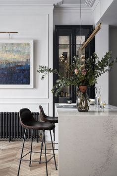 a kitchen with marble counter tops and black bar stools next to a painting on the wall