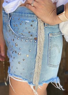 "These Levi's shorts have been given an eye-catching upgrade! Each individual strand of jewels was thoughtfully placed to create a fun fringe look. Perfect for a festival, Coachella, Stage Coach, or even just a summer vacation! This pair features various studs on the front that are straight from the Levis factory. Levis seem to run a little snug, so please check measurements for your best fit! Measurements: Waist: 30\" Rise: ~11 1/4\" Inseam: 2\"" Bohemian Embellished Bottoms For Festival, Summer Party Jean Shorts With Rhinestone Fringe, Party Shorts With Rhinestone Fringe, Cutoff Jean Shorts With Rhinestones For Summer, Summer Cutoff Jean Shorts With Rhinestones, Summer Party Shorts With Fringe, Rhinestone Fringe Shorts For Spring Party, Spring Party Shorts With Rhinestone Fringe, Rhinestone Cutoff Bottoms For Summer