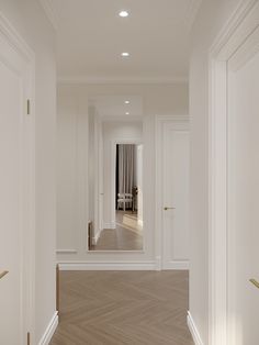 an empty hallway with white walls and wood floors, leading to a living room that has a large mirror on the wall