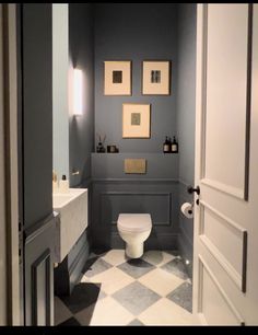 a white toilet sitting inside of a bathroom next to a sink and mirror with pictures on the wall