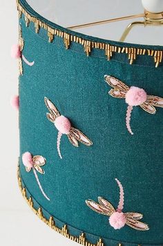 a lamp shade with dragonflies on it and pink pom - poms hanging from the side