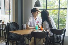 a man and woman sitting at a table in front of a window with drinks on it