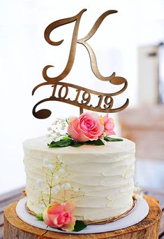 a white cake topped with a wooden monogrammed k on top of a table