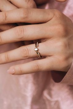 a woman's hand wearing a gold ring with a white diamond on the middle