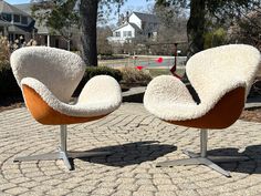 two chairs sitting next to each other on top of a brick floored area with trees in the background