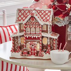 a gingerbread house decorated with icing and candy canes on a table next to a christmas tree