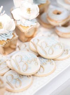 decorated cookies and cupcakes sitting on a table with white flowers in the center