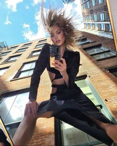 a woman taking a selfie in front of a tall building with her hair blowing in the wind