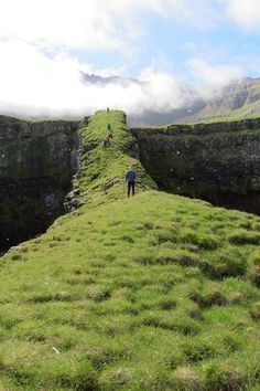 a man standing on top of a lush green hillside next to a cliff face covered in grass