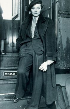 an old black and white photo of a woman sitting on a train with her hands in her pockets