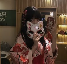 a woman wearing a geisha mask holding up her cell phone