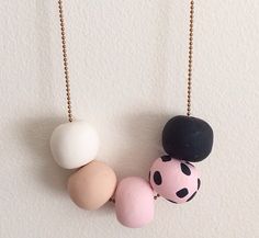 three necklaces with different colors and designs on them hanging from chains against a white wall