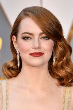 an image of a woman with red hair wearing gold dress and large earrings on the oscars red carpet