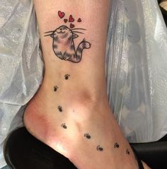 a cat tattoo on the ankle with hearts and paw prints