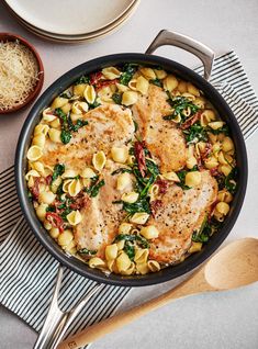 a skillet filled with chicken, pasta and spinach on top of a table