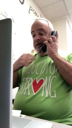 an older man talking on his cell phone while sitting in front of a laptop computer