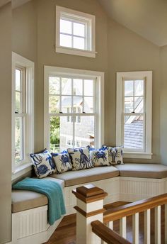 a window seat with pillows on it in front of two windows and stairs leading up to the second floor