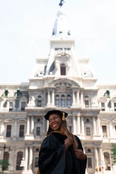 a woman in graduation gown and cap standing in front of a large building with a clock tower