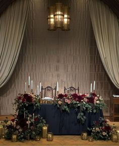 a table with candles and flowers on it in front of a curtained wall at a wedding