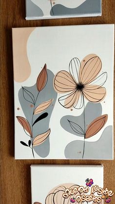 two paintings with flowers on them sitting on top of a wooden table next to each other