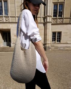 a woman walking across a street carrying a white purse on top of her shoulder and wearing black pants