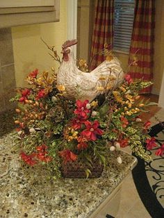 a chicken sitting on top of a counter next to a vase with flowers in it