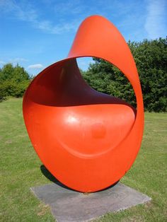 an orange sculpture sitting in the middle of a field