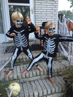 two young boys in skeleton costumes standing on steps with their hands up to the camera