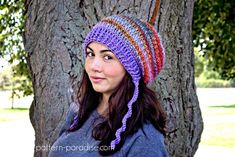 a woman standing next to a tree wearing a multicolored crocheted hat