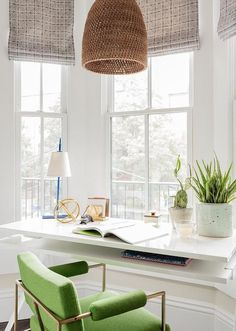 a green chair sitting in front of a window next to a desk with a book on it