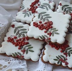 several decorated cookies with red berries and green leaves on white doily, sitting on a lace tablecloth