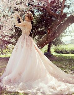 a woman in a pink dress is standing under a tree with white flowers on it