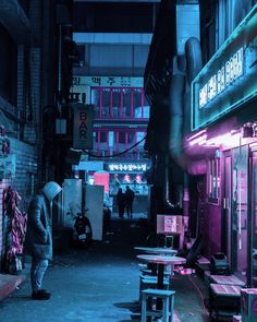 a man standing in the middle of an alley way at night with neon lights on