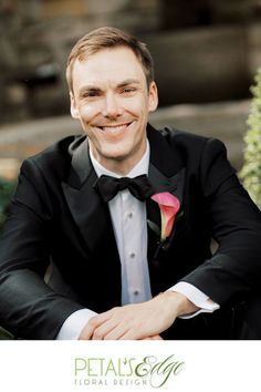 a man in a tuxedo smiles for the camera while sitting on a bench