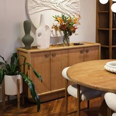 a wooden table with white chairs and vases on it in front of a mirror