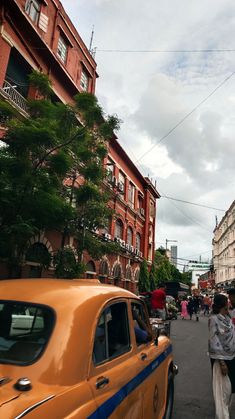 an orange taxi cab driving down a busy street next to tall buildings and people walking on the sidewalk