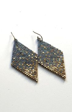 a pair of gold and blue earrings on a white surface with one earring in the shape of a triangle