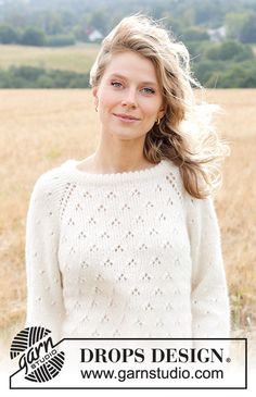 a woman standing in a field with her hair blowing in the wind and wearing a white sweater