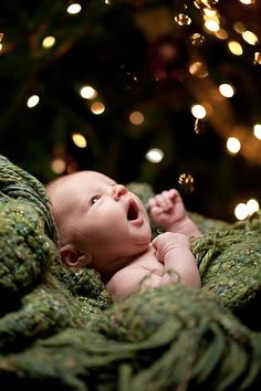 a baby laying on top of a blanket next to a christmas tree with lights in the background