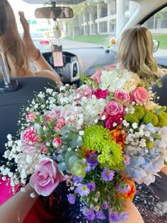 two women sitting in the back seat of a car, one holding a bouquet of flowers