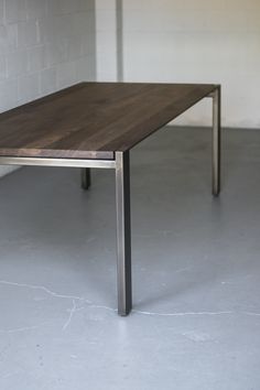 a wooden table sitting on top of a white floor next to a brick wall in an empty room