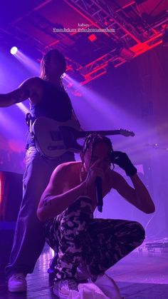 two people standing on stage with microphones in their hands and one person kneeling down