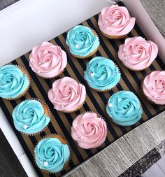 cupcakes with pink and blue frosting in a box on a wooden table