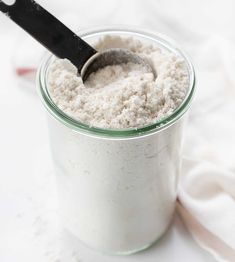 a jar filled with white powder on top of a table next to a black spoon