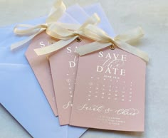 three wedding save the dates cards tied to blue envelopes with gold ribbons and bows