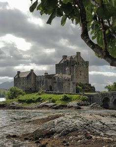 an old castle sitting on top of a lush green hillside next to a body of water