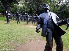 a statue of a man in a suit with many other statues behind him on the grass