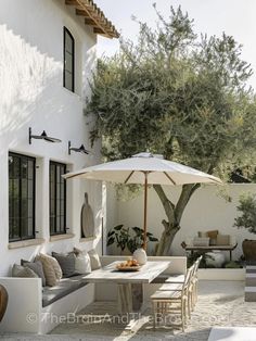 an outdoor dining area with table, chairs and umbrella in front of a white house