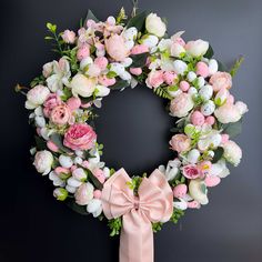 a wreath with pink and white flowers is hanging on a black wall next to a bow