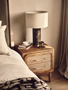 a nightstand with a lamp on top of it next to a bed in a bedroom